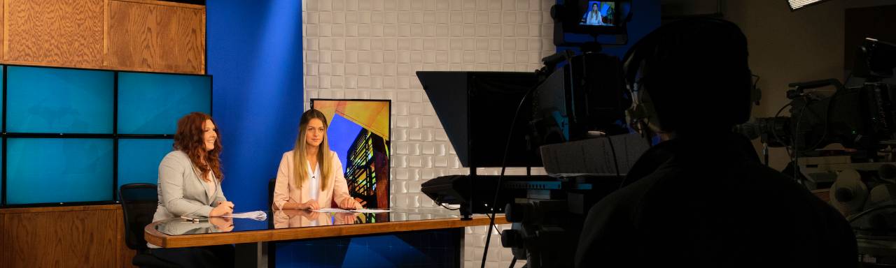 2 student sitting at anchor desk in TV studio